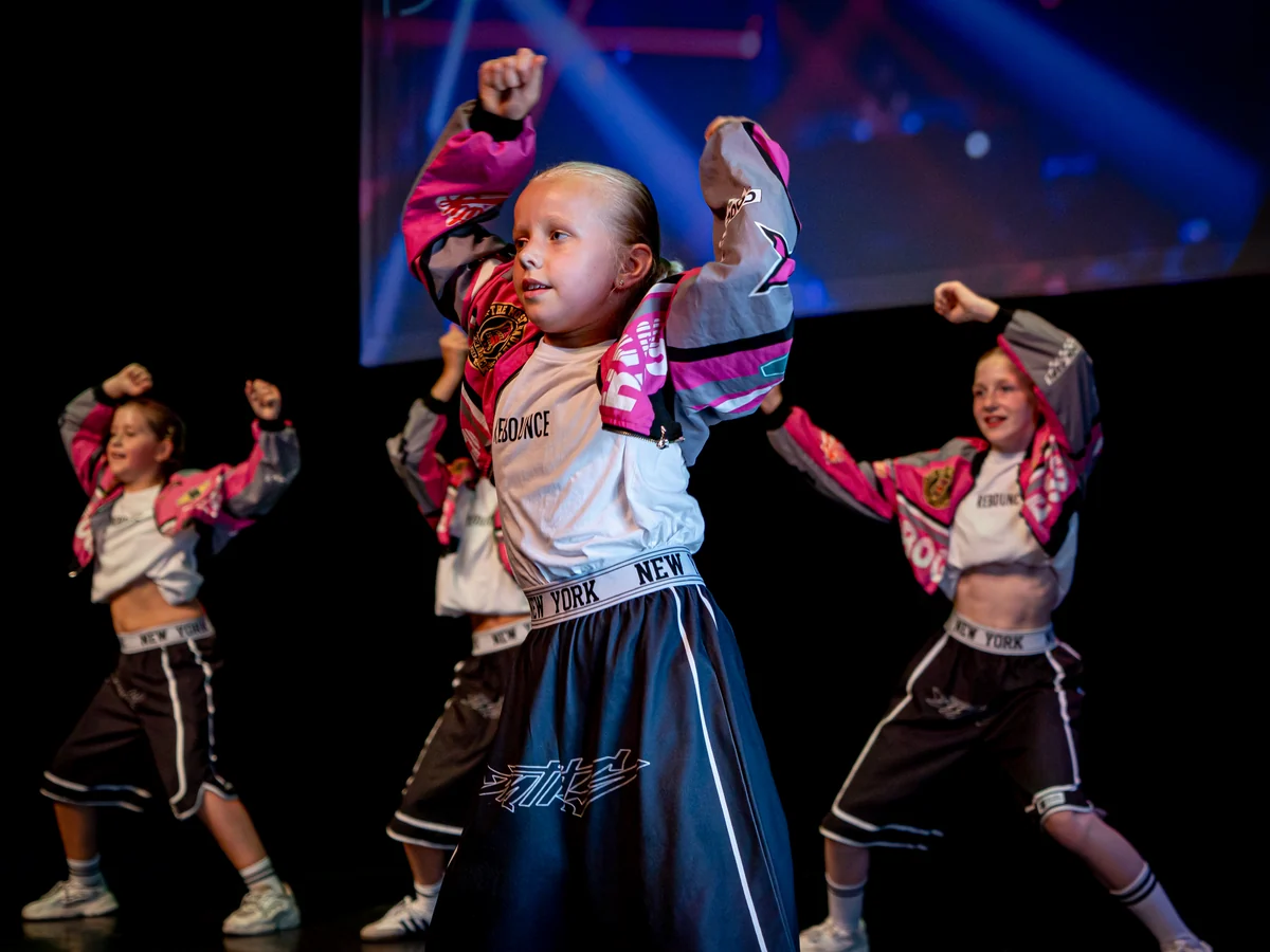 Jonge Rebounce-dansers in roze jasjes dansen met opgeheven armen tijdens de eindvoorstelling